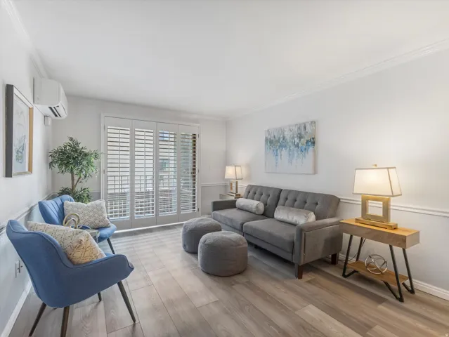 Living area featuring wood-finish flooring, white walls with crown molding, and sliding glass doors with plantation shutters