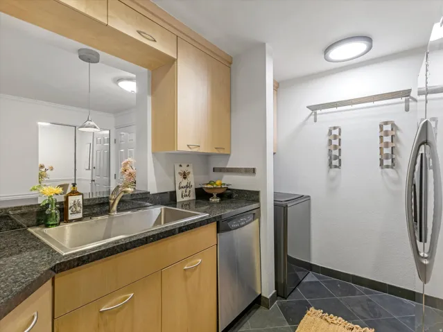 Kitchenette featuring light wood-finish cabinetry, dark speckled countertops, and a stainless steel sink
