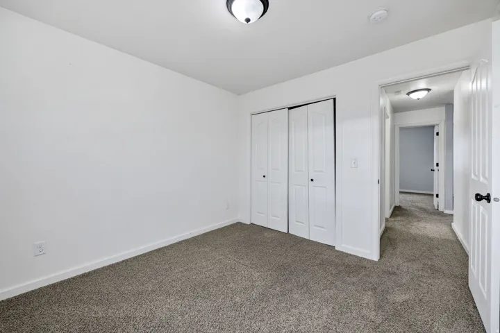 Neutral-toned carpet flooring and white walls define this space, featuring a double bi-fold closet