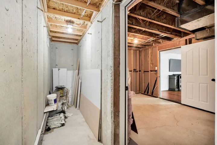 Unfinished basement area featuring concrete walls and flooring, exposed ceiling joists, and a partial wood-framed wall