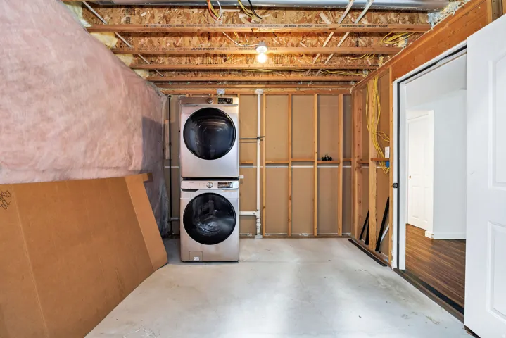 Laundry area featuring a stacked stainless steel washer and dryer, concrete flooring, and exposed ceiling joists