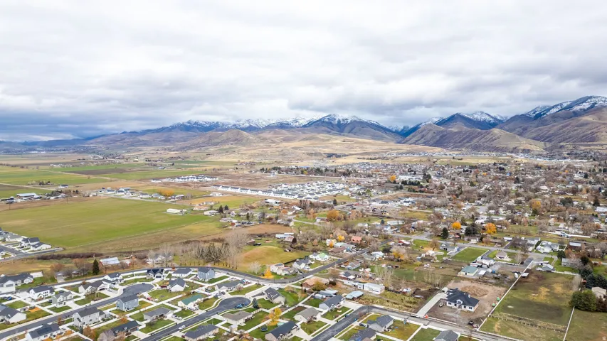 Aerial perspective showcasing an expansive residential area with varied housing styles, surrounded by open fields and distant snow-capped mountains