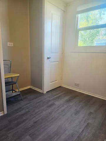 Room featuring wood-finish flooring, a white paneled door, and a window providing natural light
