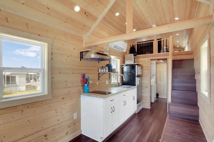 Compact kitchen featuring white cabinetry with dark hardware, a stainless steel sink, and light-toned countertops