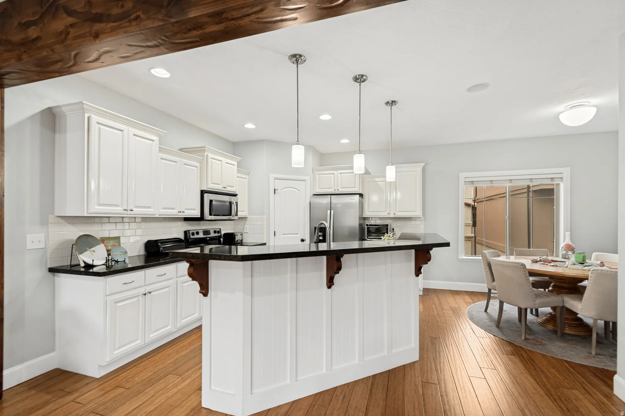 Kitchen featuring white shaker-style cabinetry, dark countertops, a stainless steel refrigerator, and wood-finish flooring