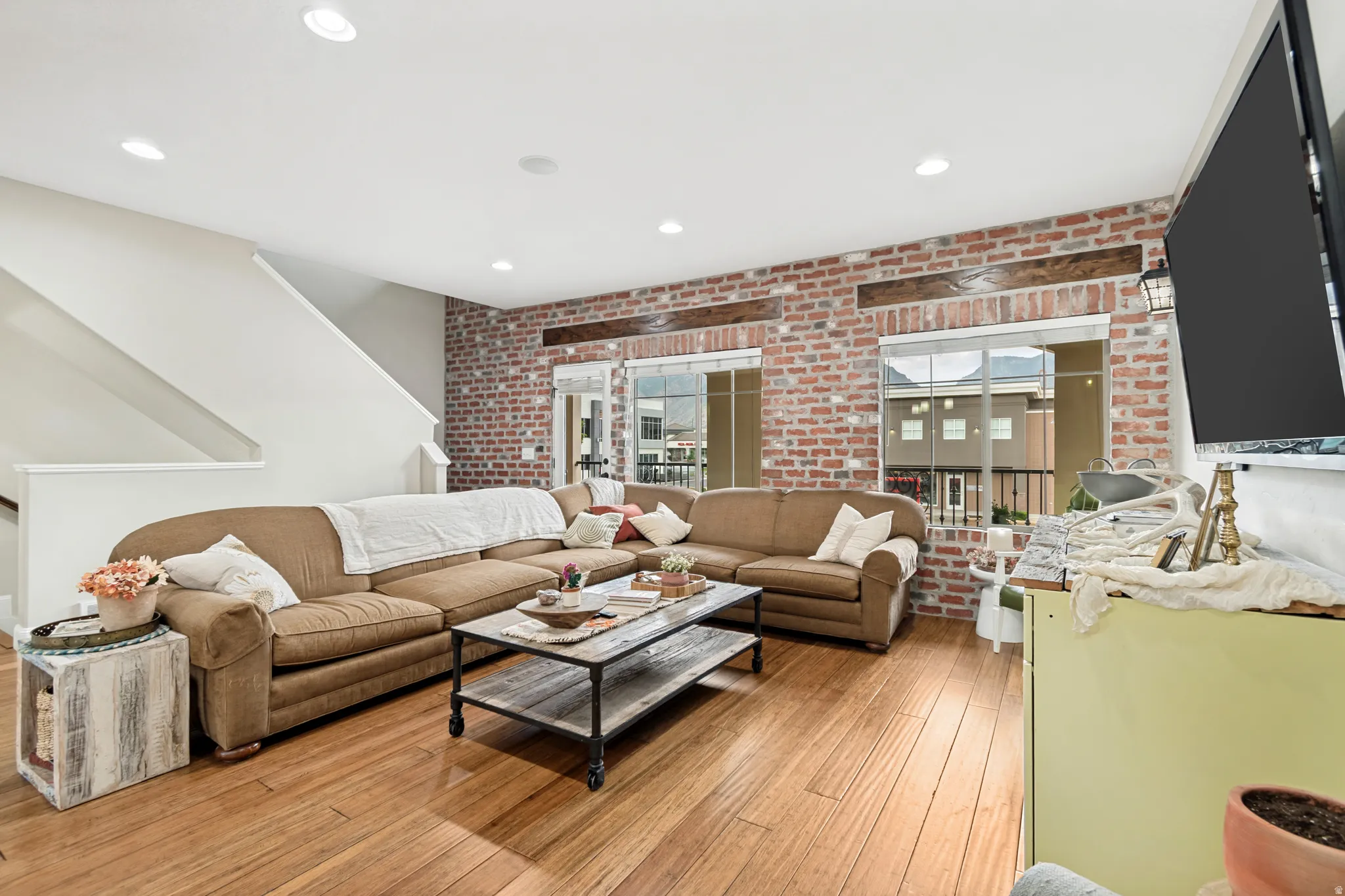 Open-concept living space with wood-finish flooring, exposed brick accent wall, and recessed lighting