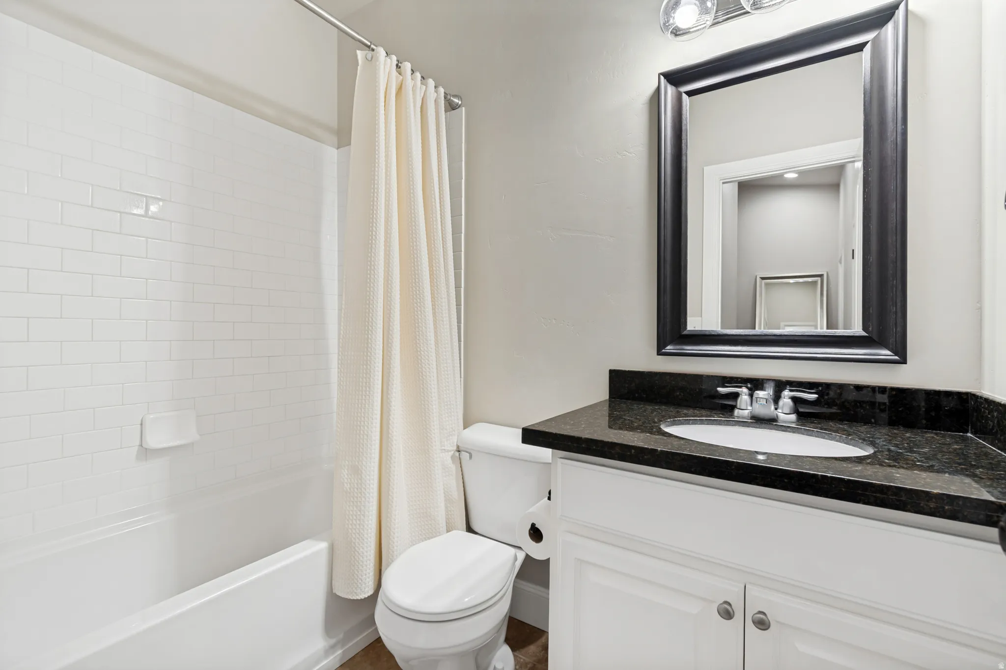 Bathroom featuring a white subway tile shower surround, a white vanity with an undermount sink, dark speckled countertop, and a framed wall mirror
