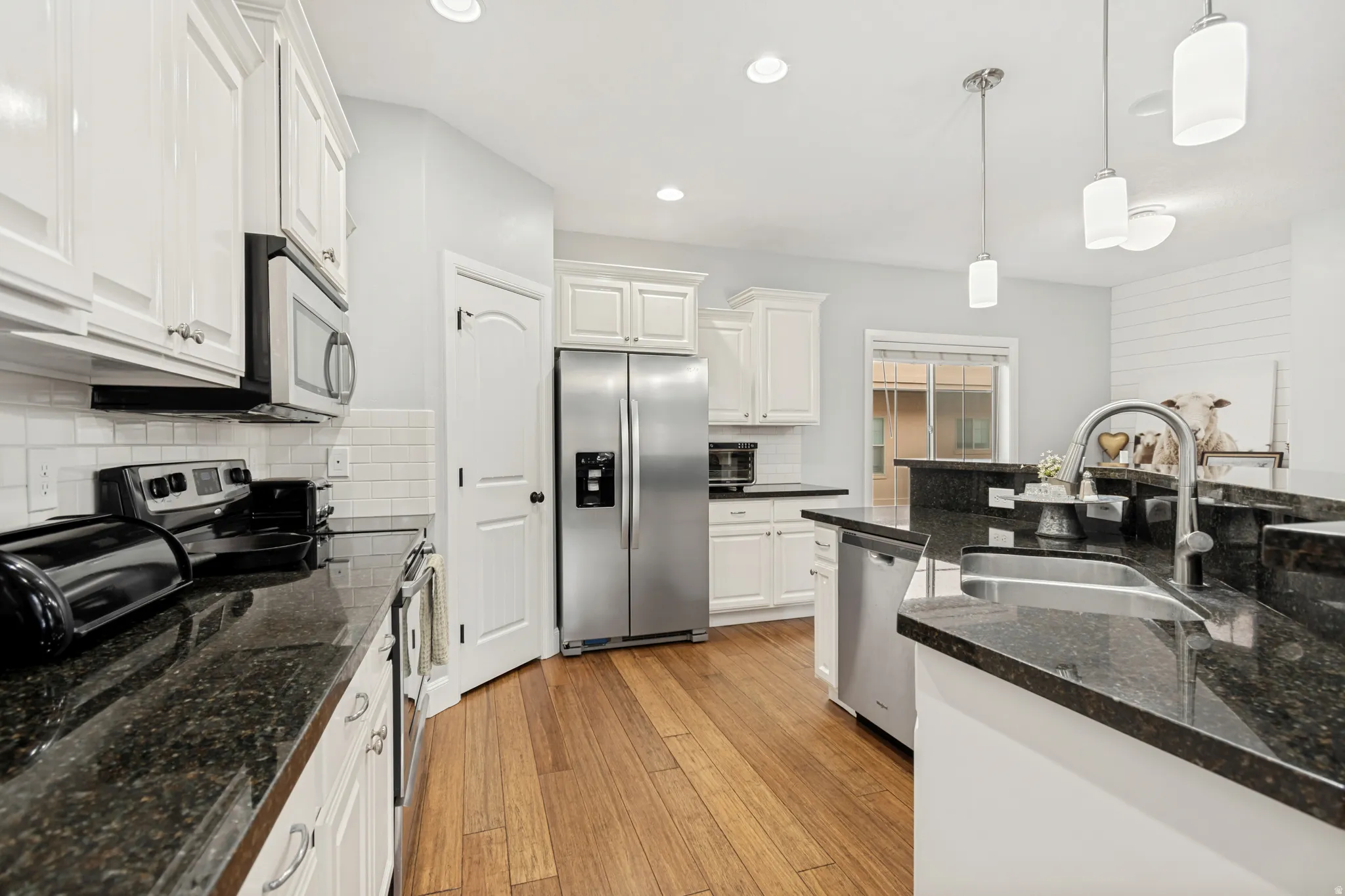Kitchen featuring white cabinetry, stainless steel appliances, dark stone countertops, wood-finish flooring, and subway tile backsplash