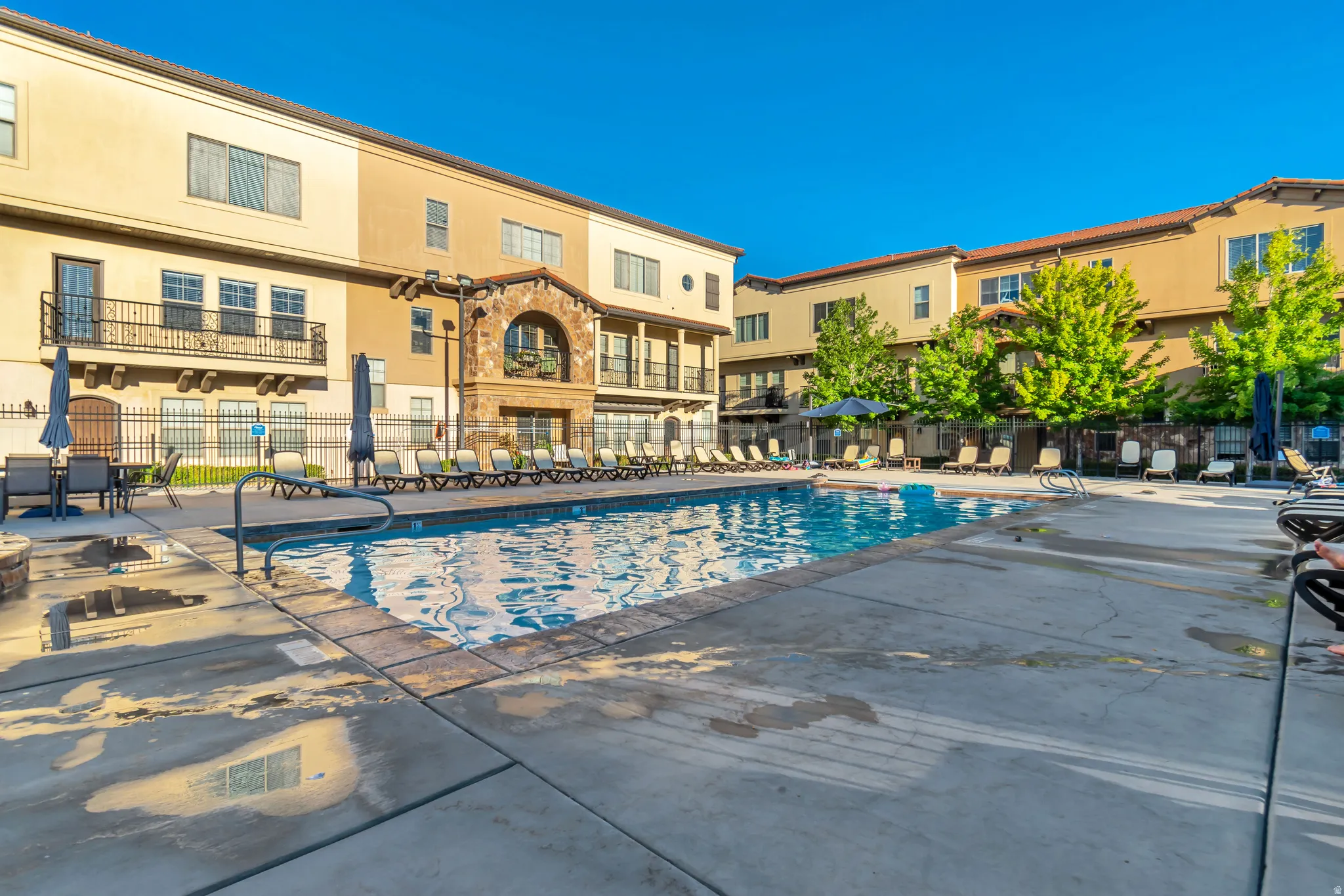 Resort-style pool area featuring a perimeter of lounge chairs, concrete decking, and mature trees