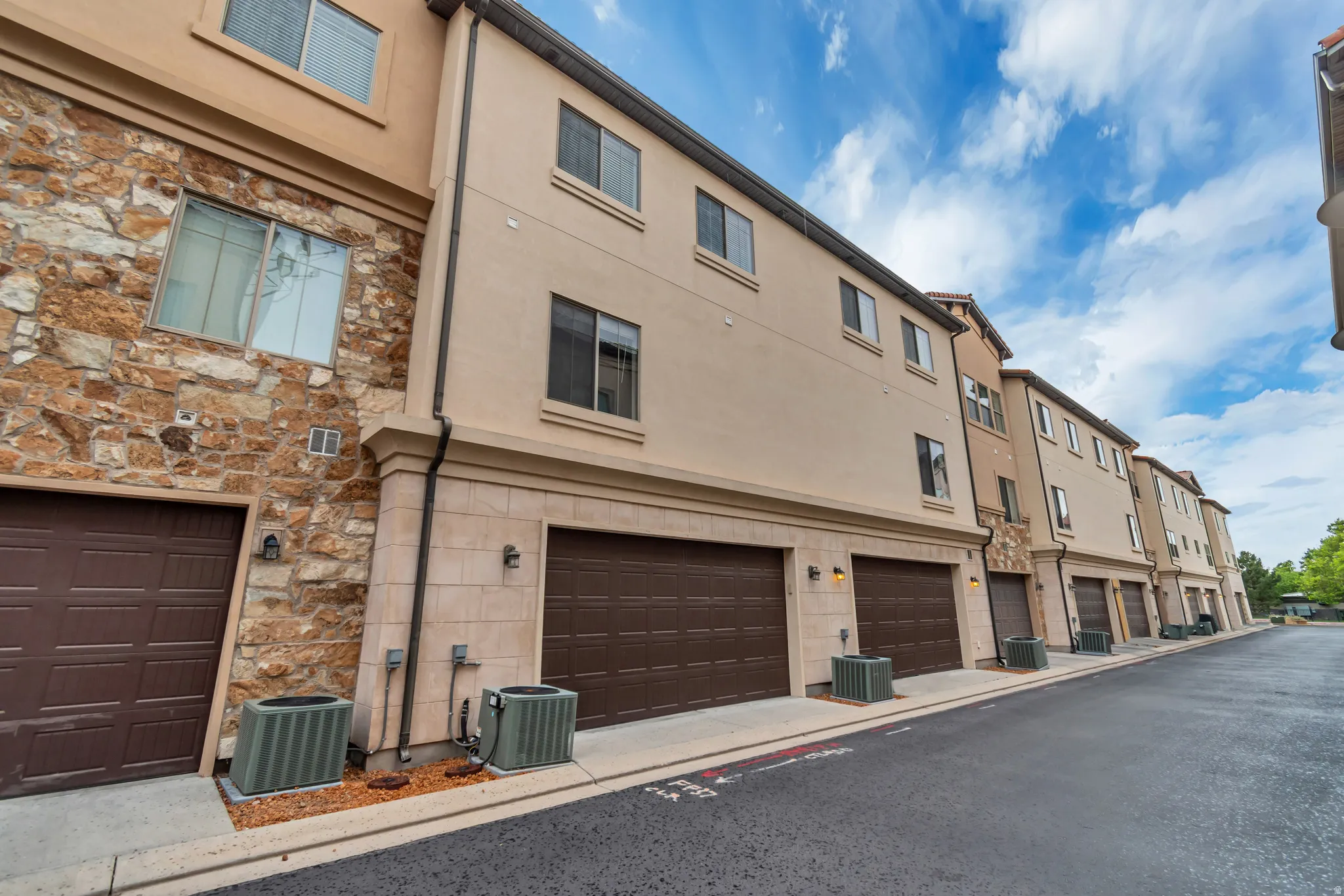 Multi-level townhome featuring a stucco and stone facade, private two-car garage, and multiple window placements