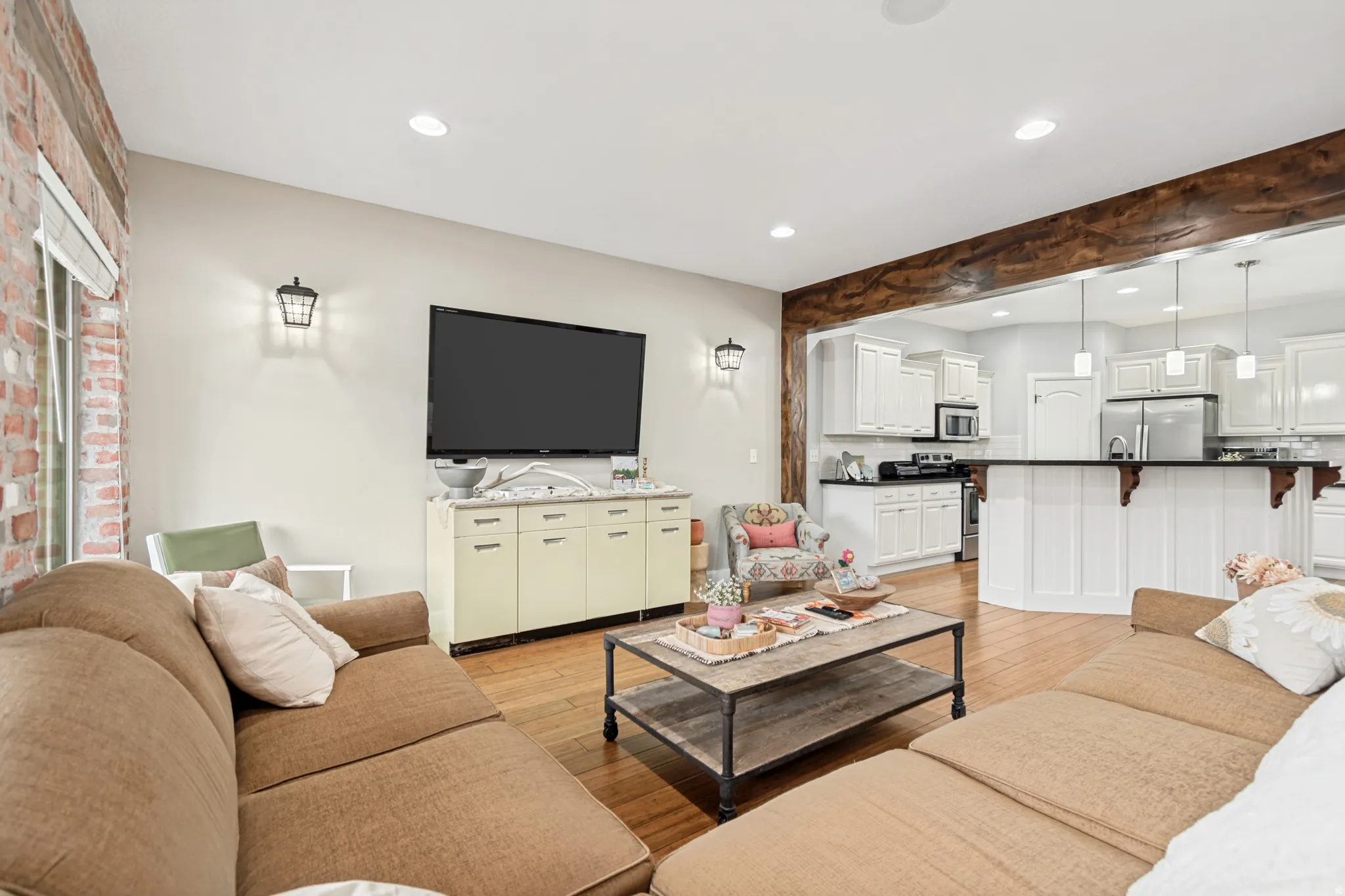 Open-concept living space featuring wood-finish flooring, a brick accent wall, and recessed lighting