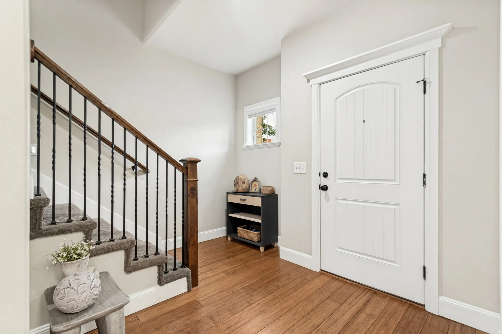 Entryway featuring wood-finish flooring, a white paneled door with an arched top panel, and a staircase with carpeted treads, dark wood handrails, and wrought iron balusters