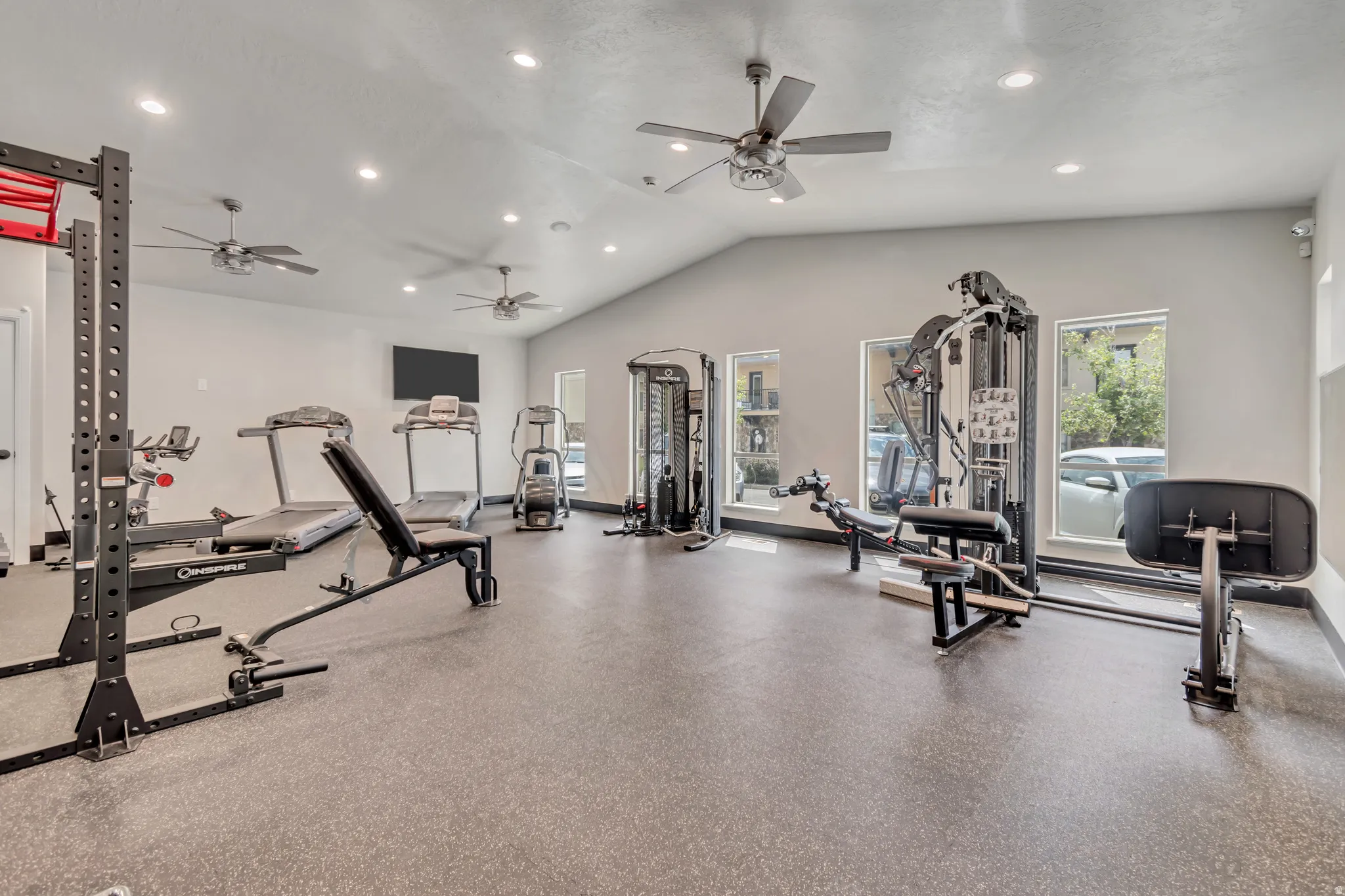 Dedicated fitness facility featuring specialized rubber flooring, ample natural light from multiple windows, and a vaulted ceiling with recessed lighting and ceiling fans