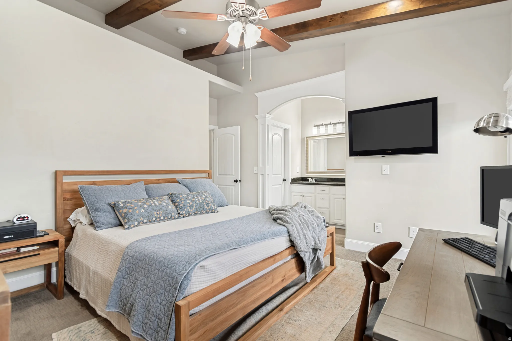 Bedroom featuring a wood-finish ceiling fan, exposed wood beams, and an arched doorway leading to a bathroom