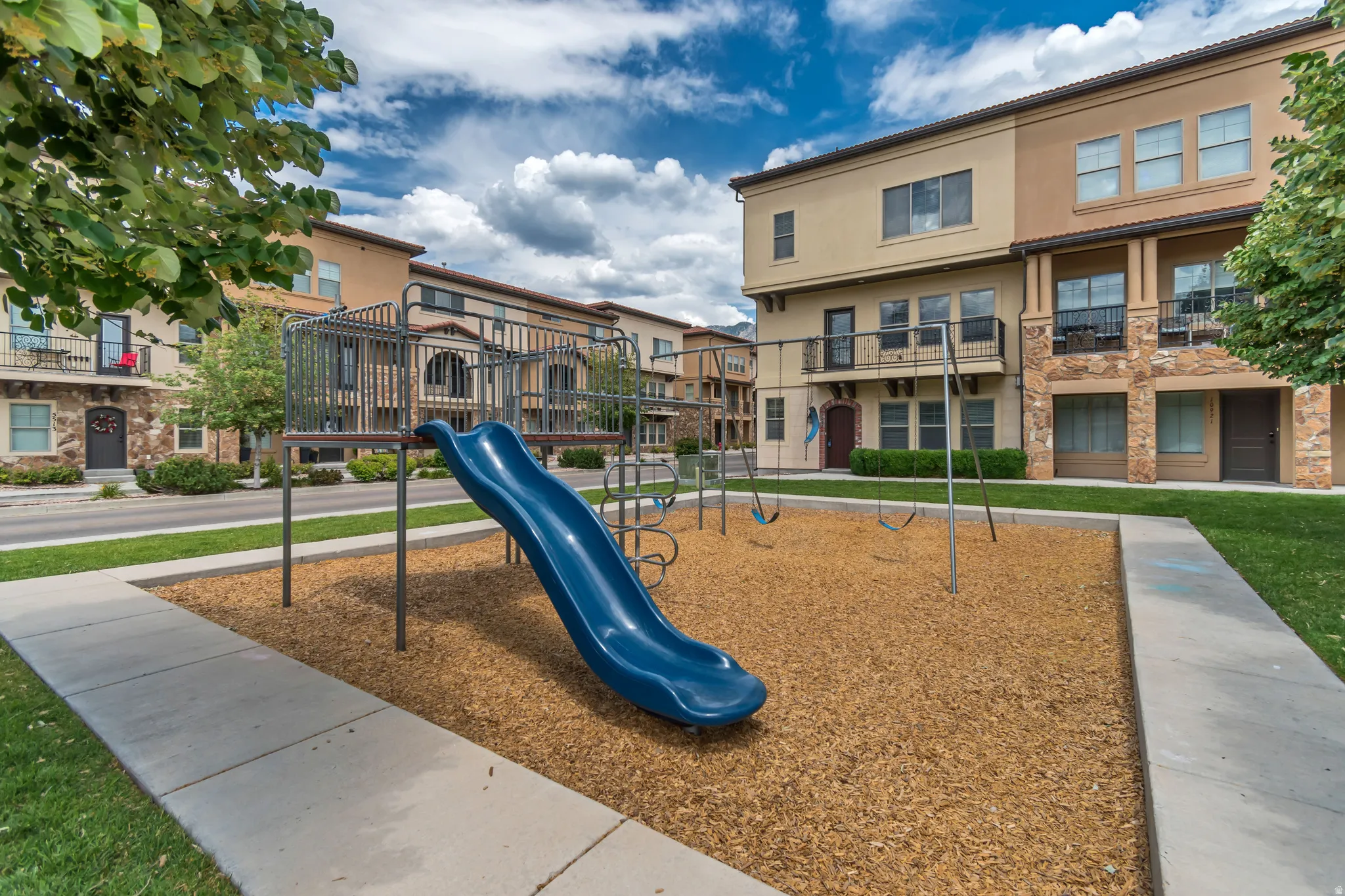 Community playground featuring a blue slide, swing set, and wood chip ground cover
