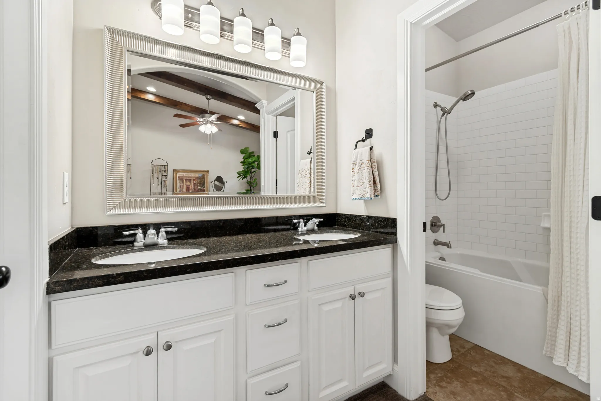 Bathroom vanity featuring dual undermount sinks, a dark countertop, and white cabinetry with brushed nickel hardware