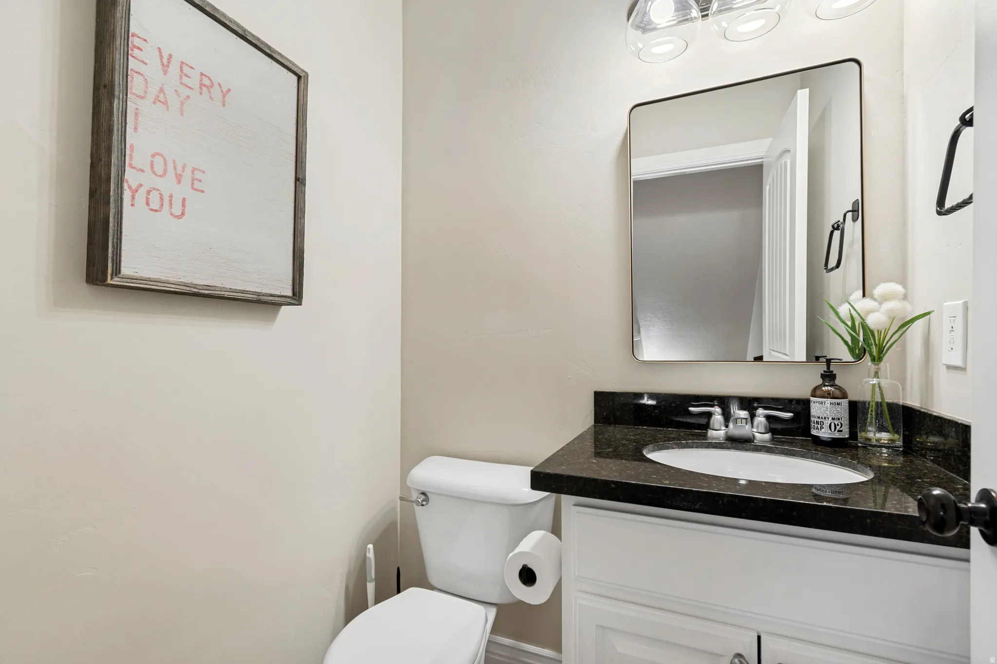 Bathroom featuring a white vanity with a dark countertop, an undermount sink with a chrome faucet, a rectangular framed mirror, and clear glass vanity lighting