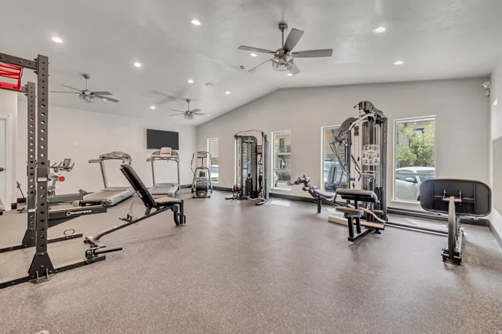 Dedicated fitness facility featuring specialized rubber flooring, ample natural light from multiple windows, and a vaulted ceiling with recessed lighting and ceiling fans