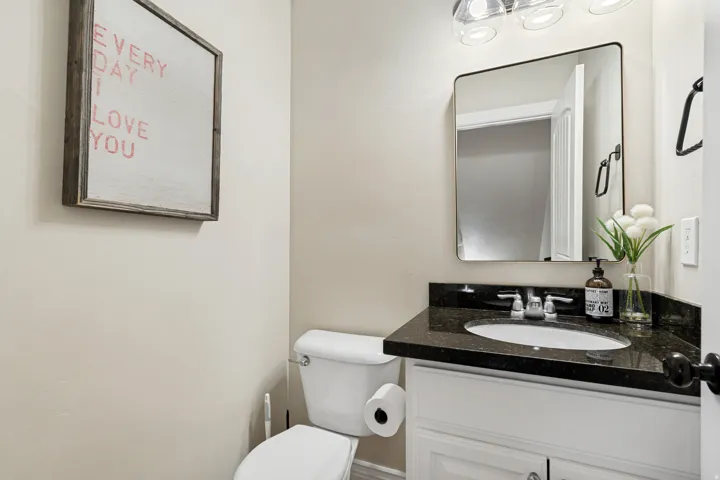 Bathroom featuring a white vanity with a dark countertop, an undermount sink with a chrome faucet, a rectangular framed mirror, and clear glass vanity lighting