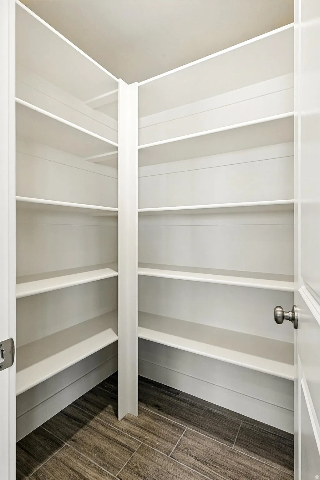 Walk-in pantry featuring built-in shelving, wood-finish flooring, and a brushed nickel doorknob