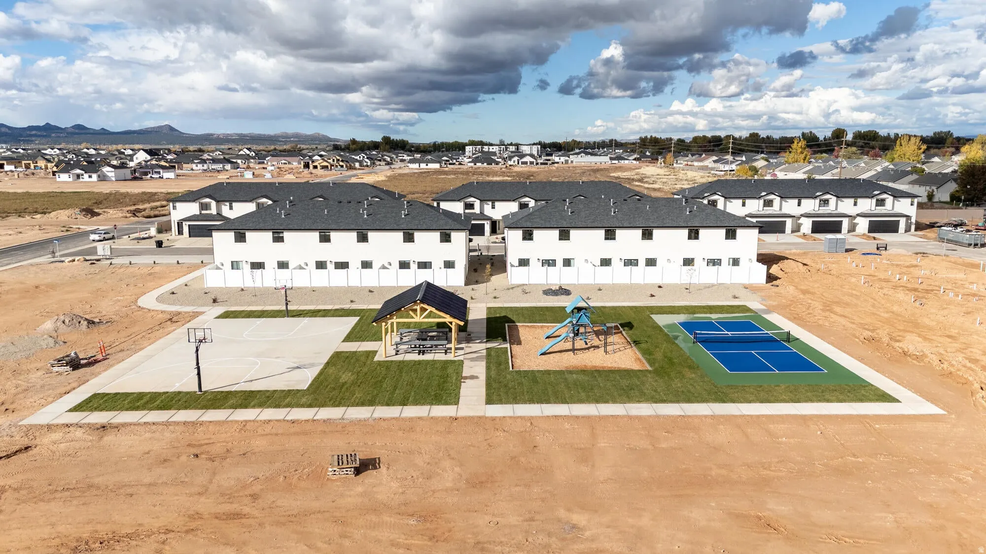 Community amenity area featuring a basketball court, covered pavilion, playground structure, and a pickleball court