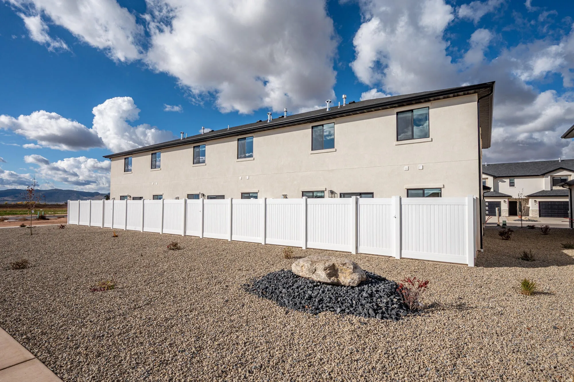 Rear stucco exterior with a dark roofline, multiple windows, and a white privacy fence