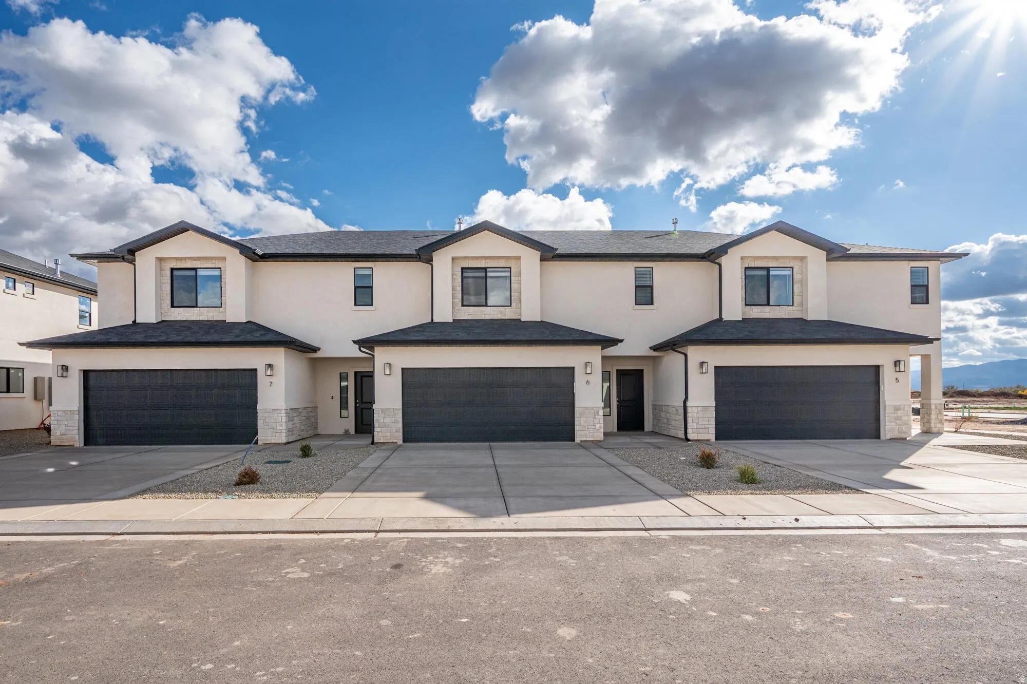 Contemporary multi-unit exterior featuring light-colored stucco, dark garage doors, and complementary stone accents