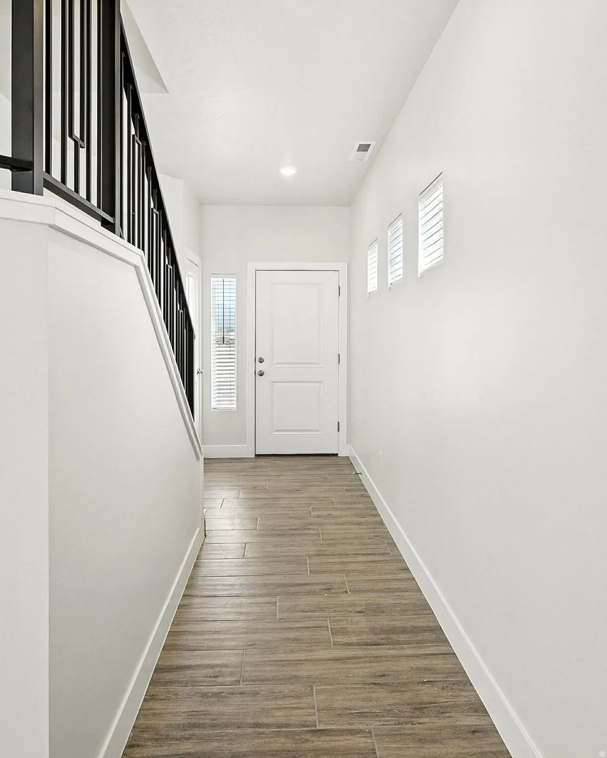 Entryway featuring wood-finish flooring, a white paneled door with sidelight, and a staircase with black metal balusters