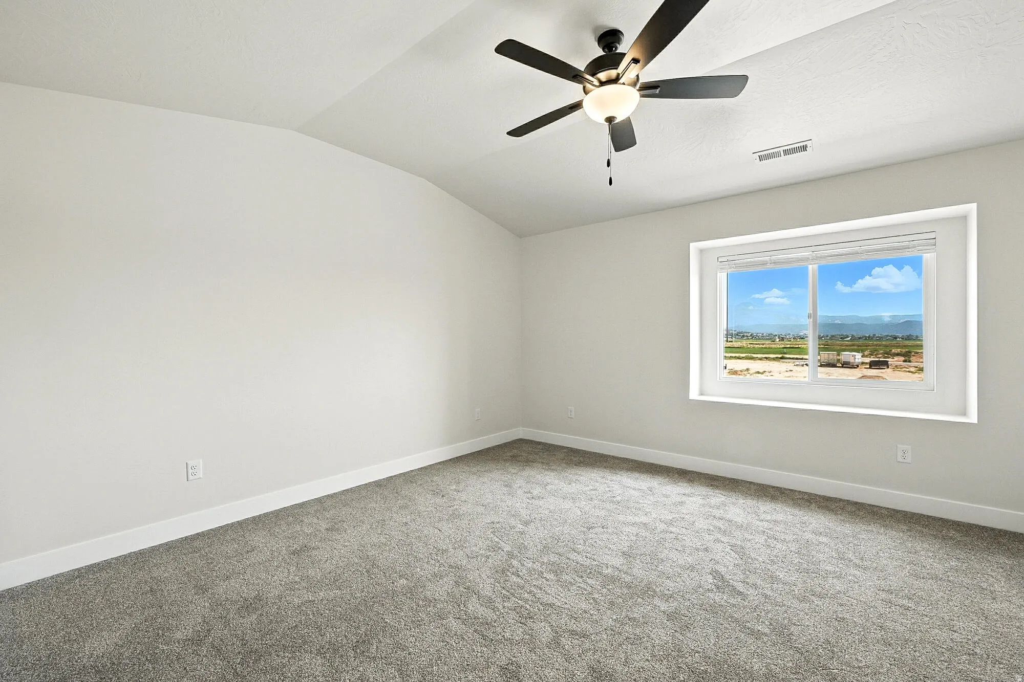 Spacious room featuring vaulted ceilings, a contemporary ceiling fan with integrated lighting, plush grey carpeting, and a large window offering expansive outdoor scenery