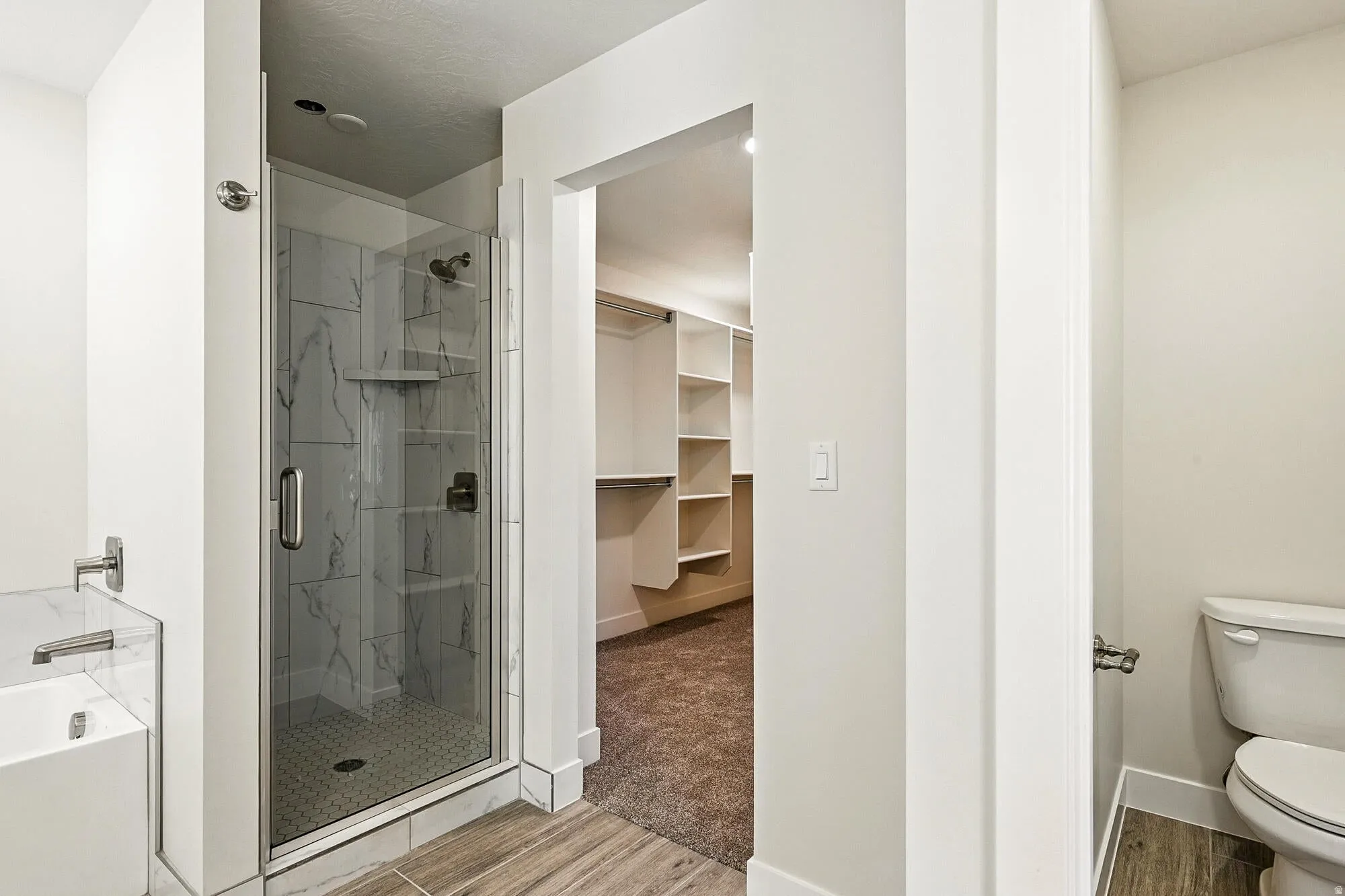 Bathroom featuring a glass-enclosed shower with large format marble-look tile, a built-in tub with marble-look surround, and wood-finish flooring