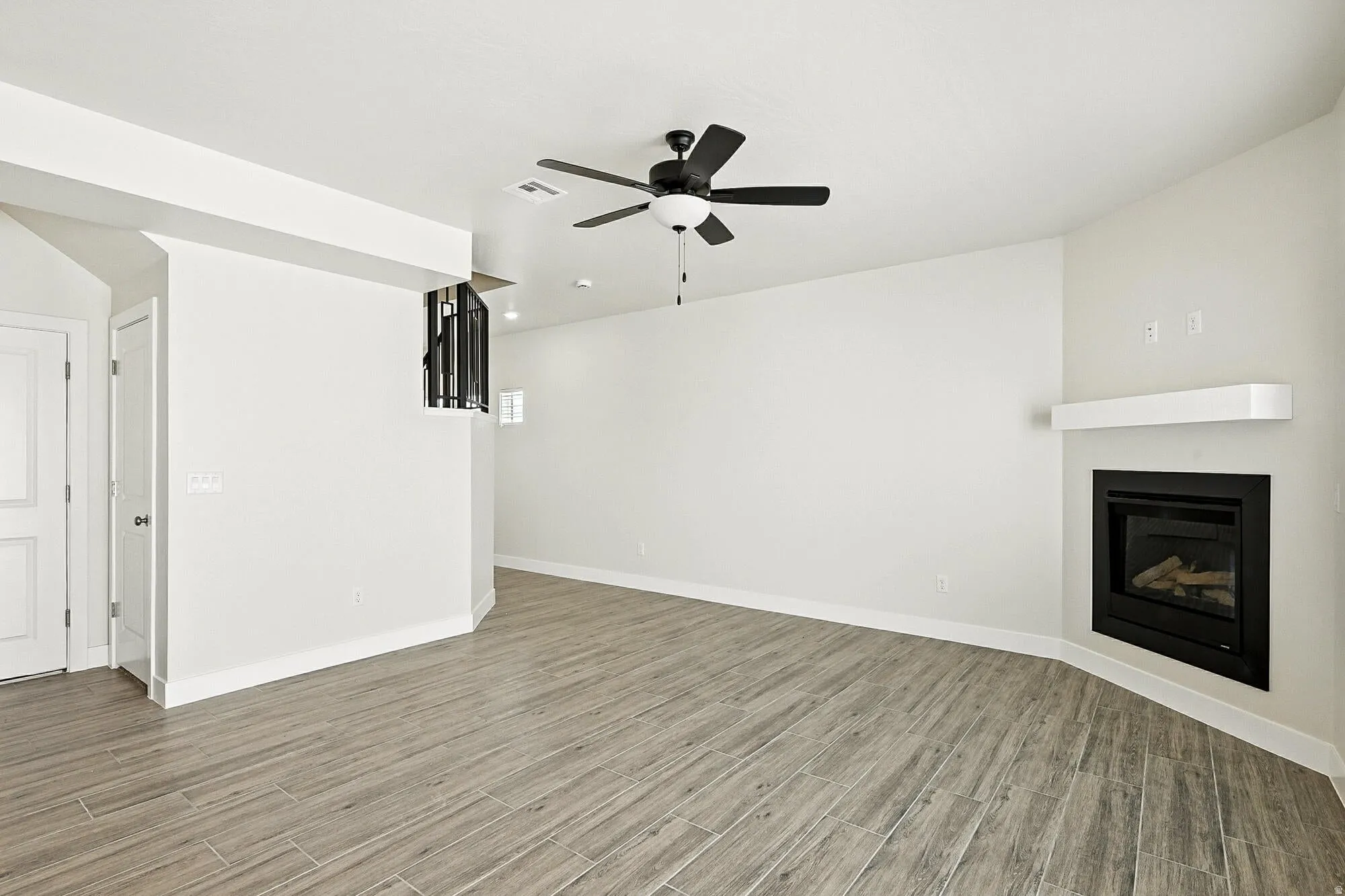Open concept living space featuring wood-finish flooring, a contemporary ceiling fan, and a built-in fireplace with a white mantel