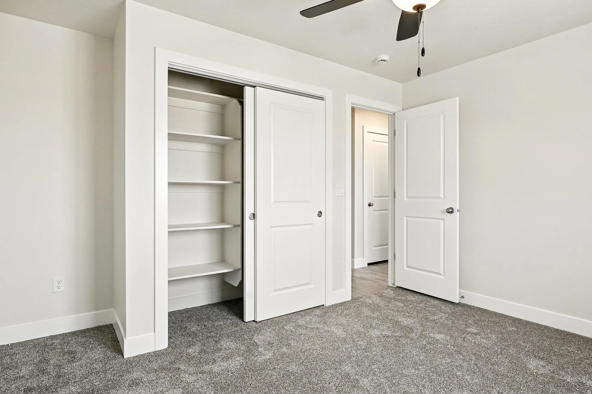 Bedroom featuring light gray wall paint, gray carpeting, a built-in closet with shelving, a ceiling fan with light fixture, and white trim