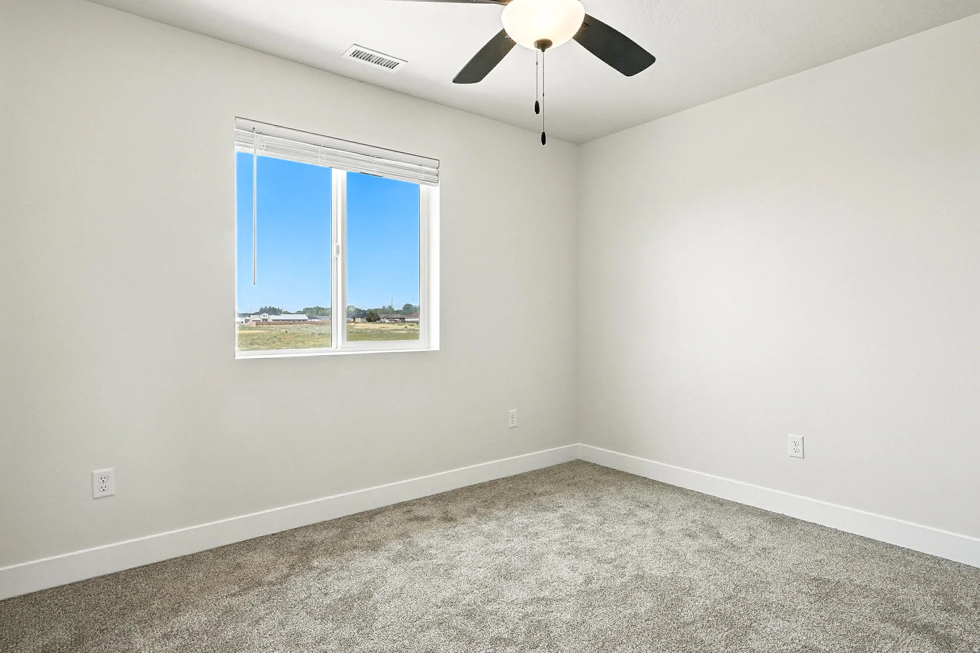 Carpeted room featuring a white window frame, white walls, and a ceiling fan with a light fixture
