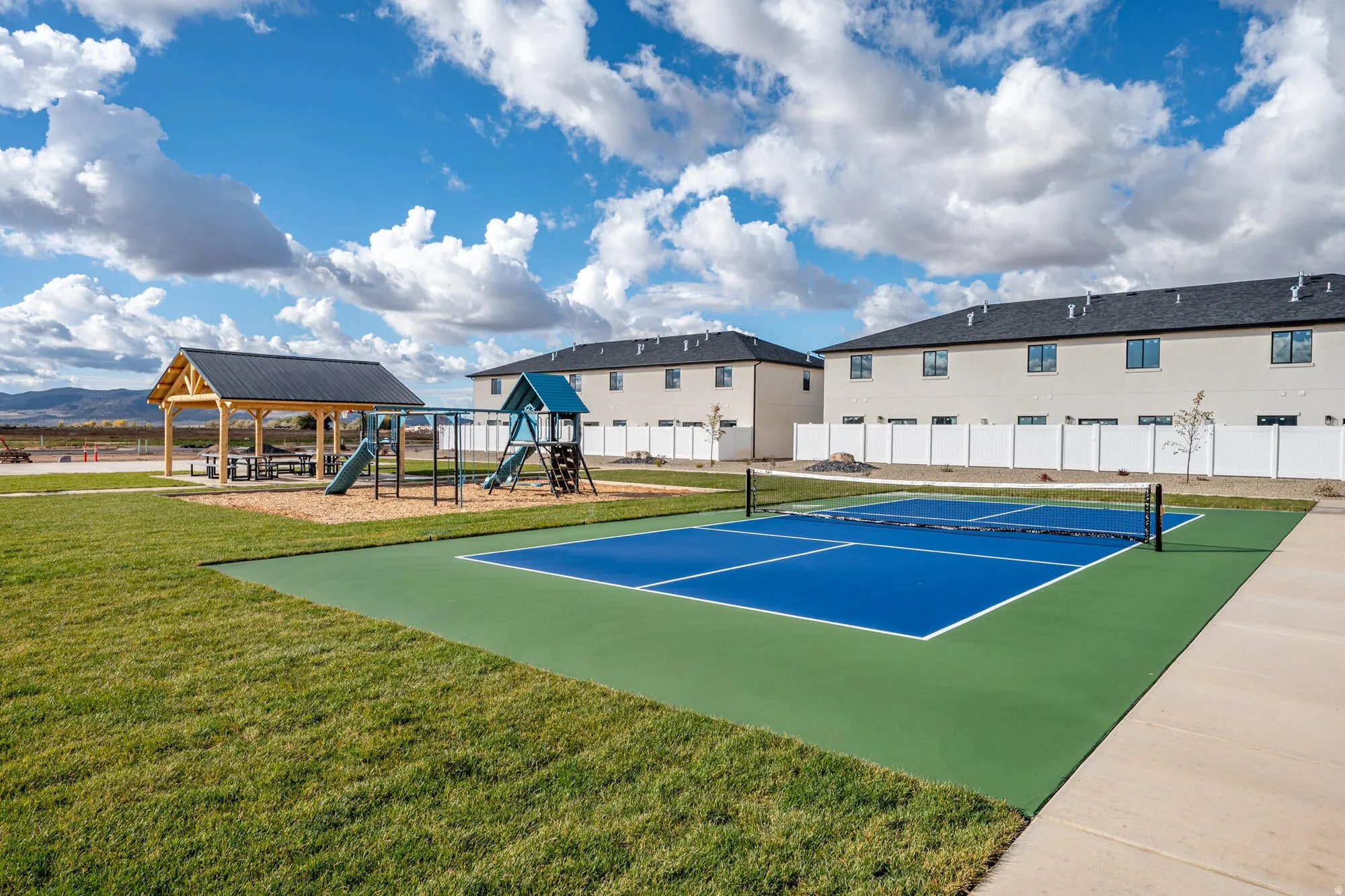 Outdoor amenity area featuring a blue and green multi-sport court, a covered pavilion with picnic tables, and a playground with slides and swings