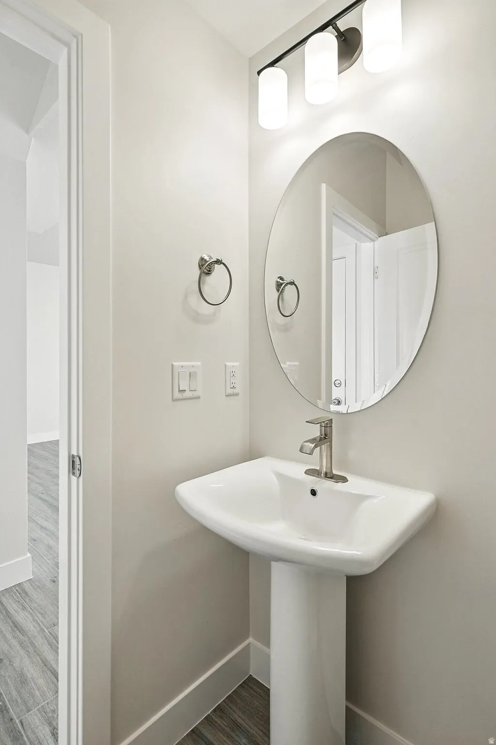 Pedestal sink with brushed nickel faucet, an oval mirror, and a three-light vanity fixture