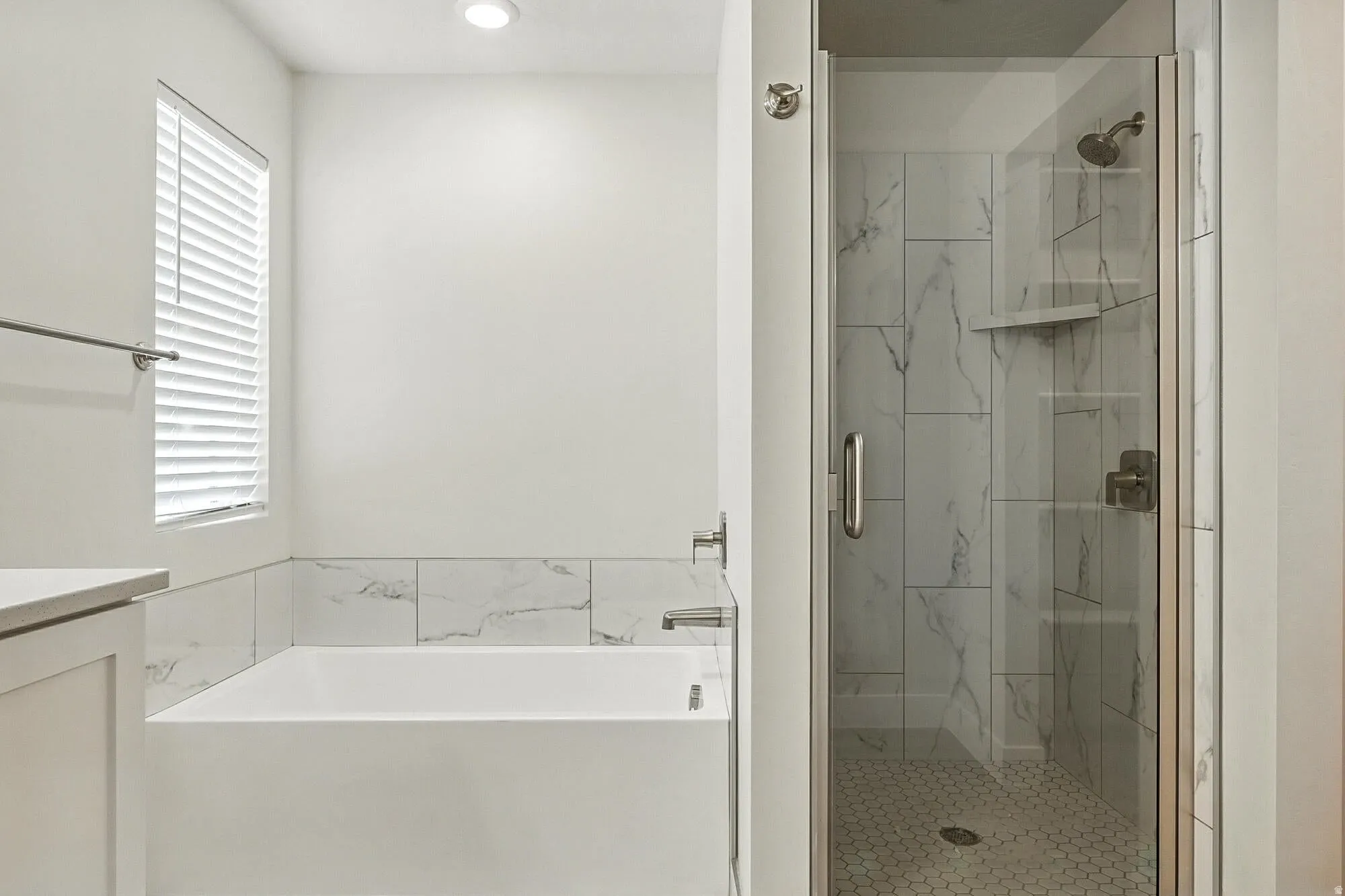 Full bathroom featuring a rectangular soaking tub with tile surround, a separate glass-enclosed shower with large format wall tiles and hexagonal floor tiles, and recessed lighting