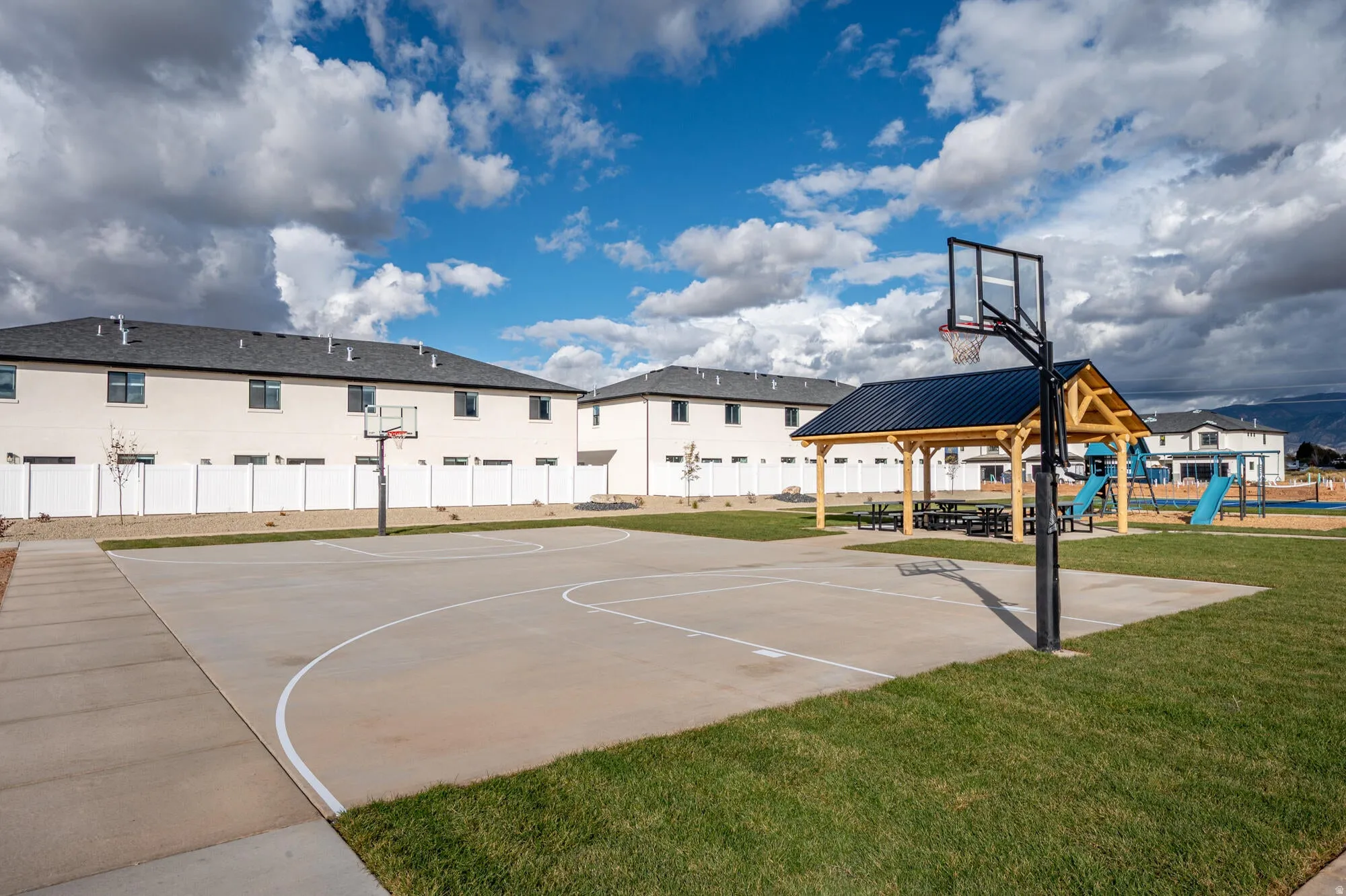 Outdoor recreational area featuring a concrete basketball half-court, a covered picnic pavilion, and expansive green spaces