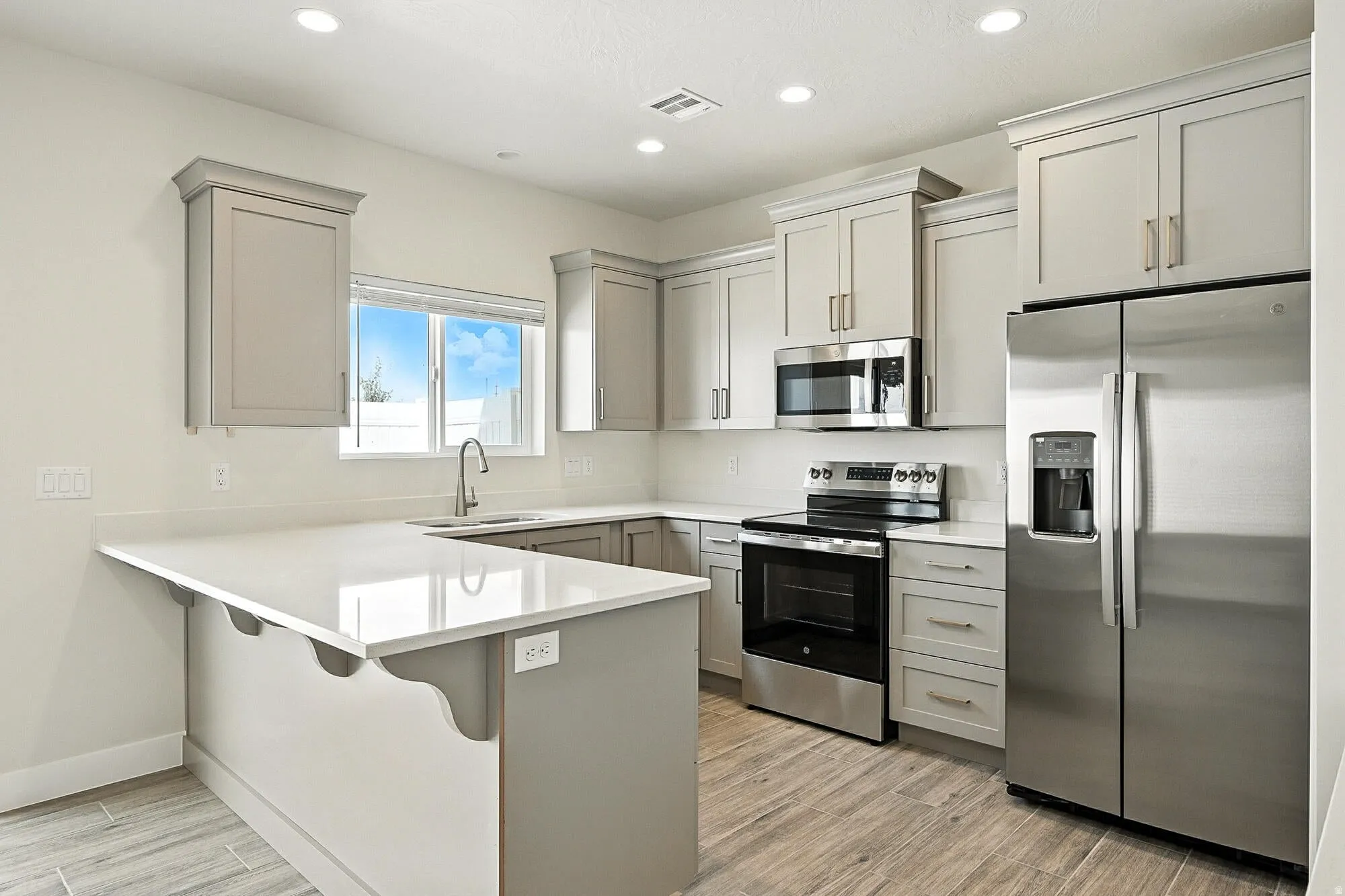 Kitchen featuring light gray cabinetry, stainless steel appliances, white countertops, and wood-finish flooring