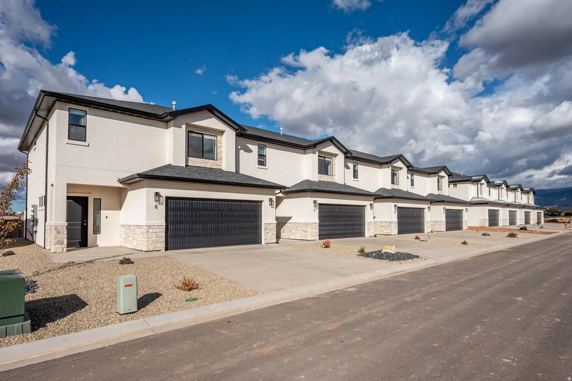 Contemporary townhome exterior with light stucco and stone facade accents, featuring a prominent black garage door