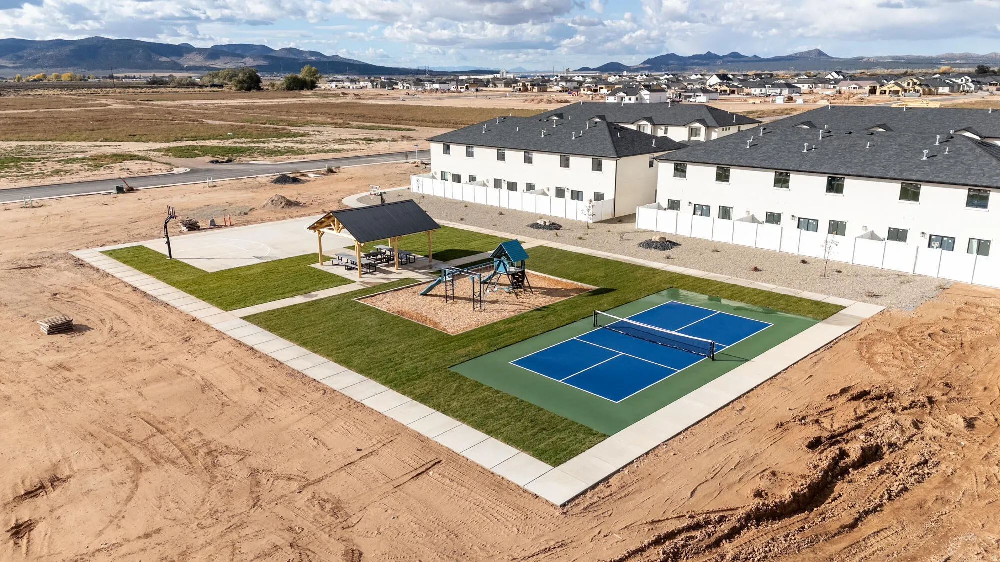 Recreational area featuring a pickleball court, basketball court, shaded picnic area, playground, and manicured lawn