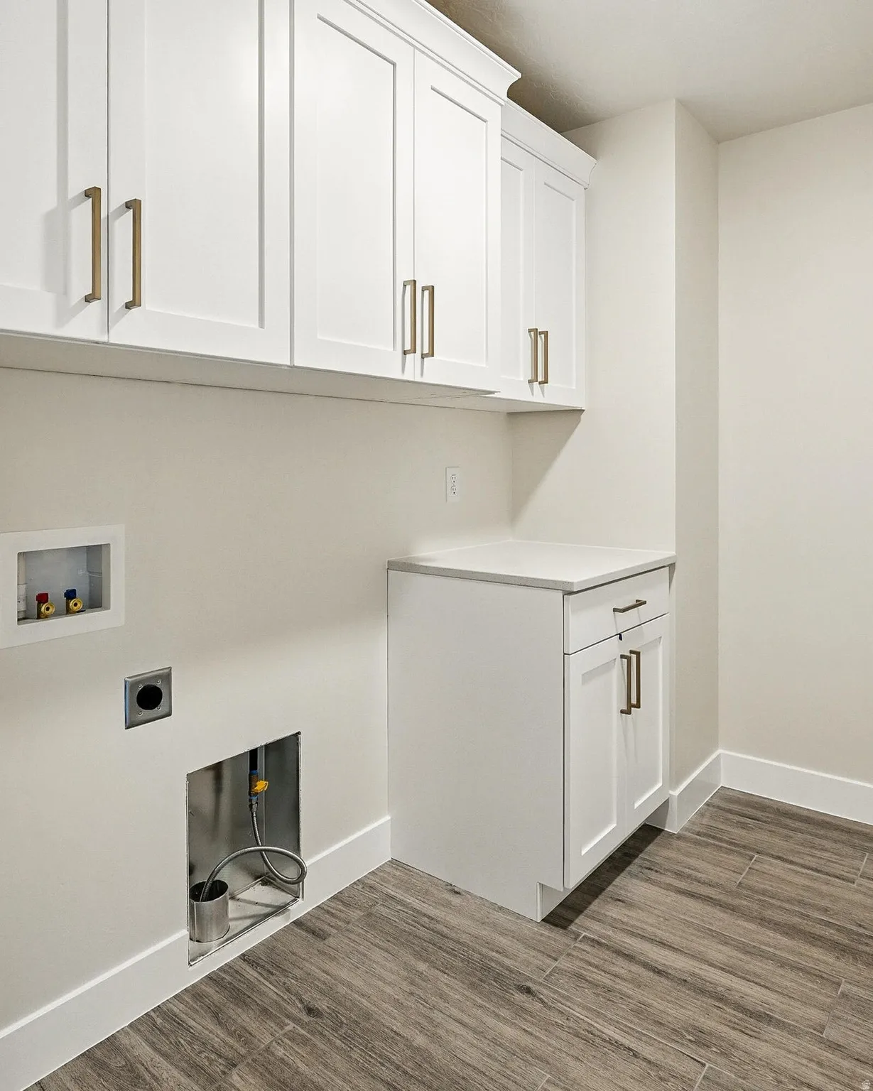 Utility room featuring white shaker-style cabinetry with gold-tone hardware, a light-toned countertop, and wood-finish tile flooring