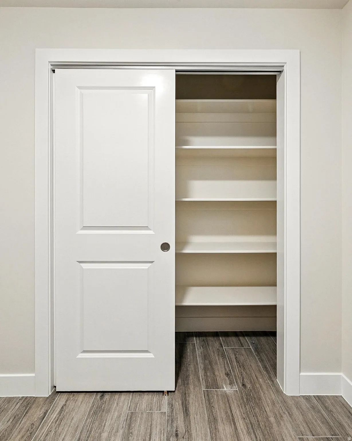 White sliding bypass closet doors with a multi-panel design, interior shelving, wood-finish flooring, and white baseboards
