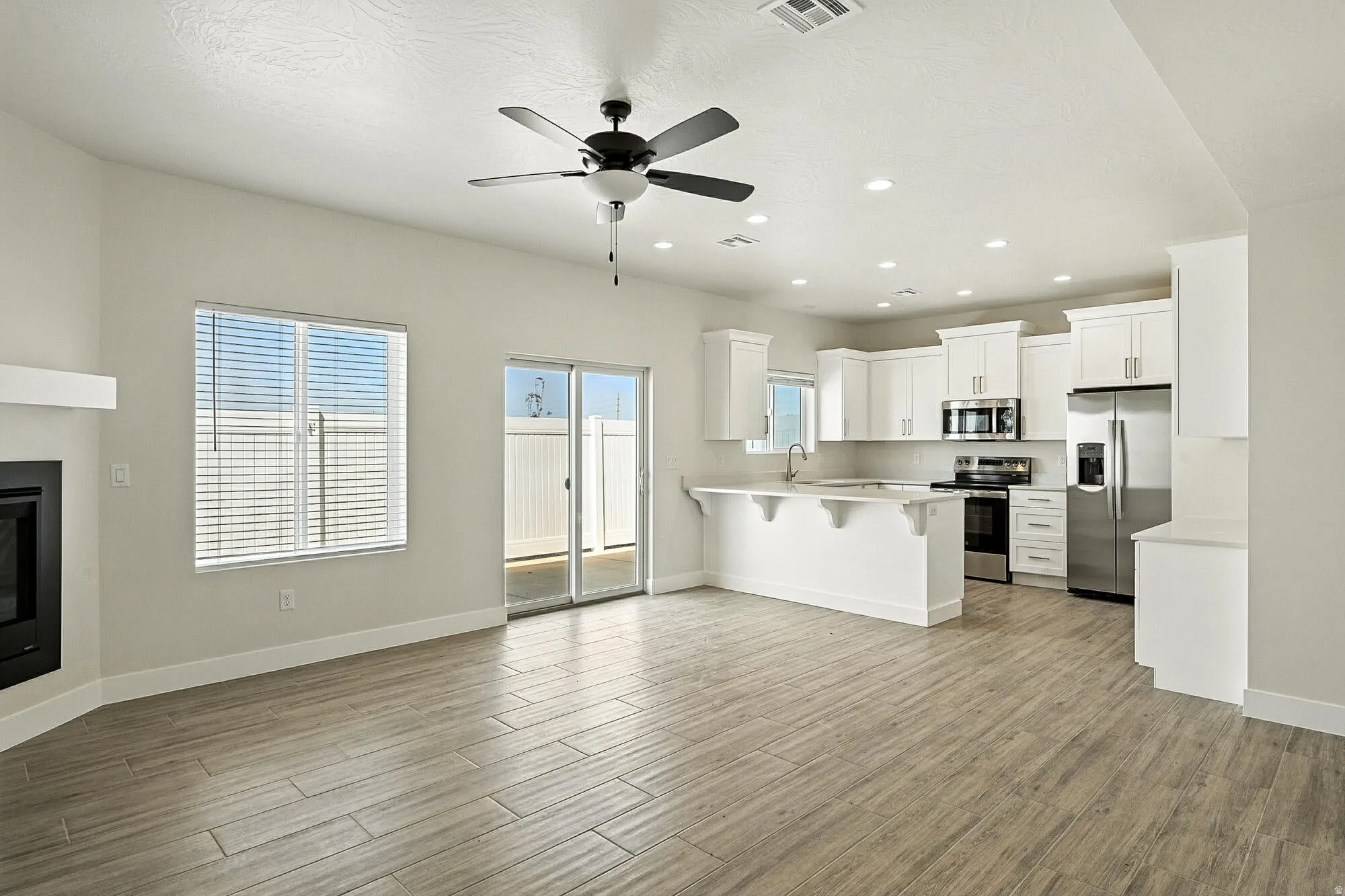 Open-concept living area with wood-finish flooring, a contemporary ceiling fan, and recessed lighting