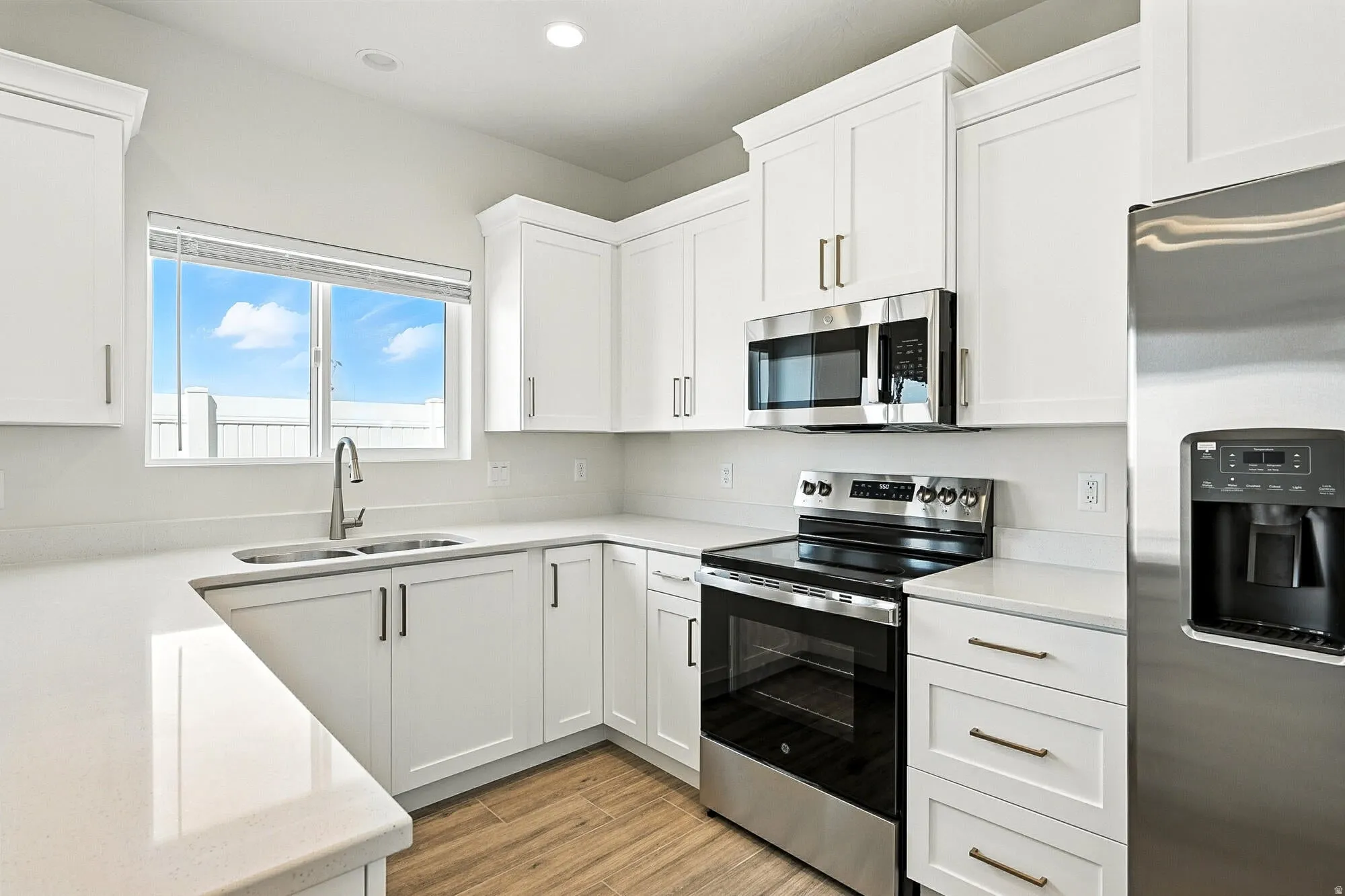 Modern kitchen featuring white cabinetry, light countertops, stainless steel appliances, and wood-finish flooring