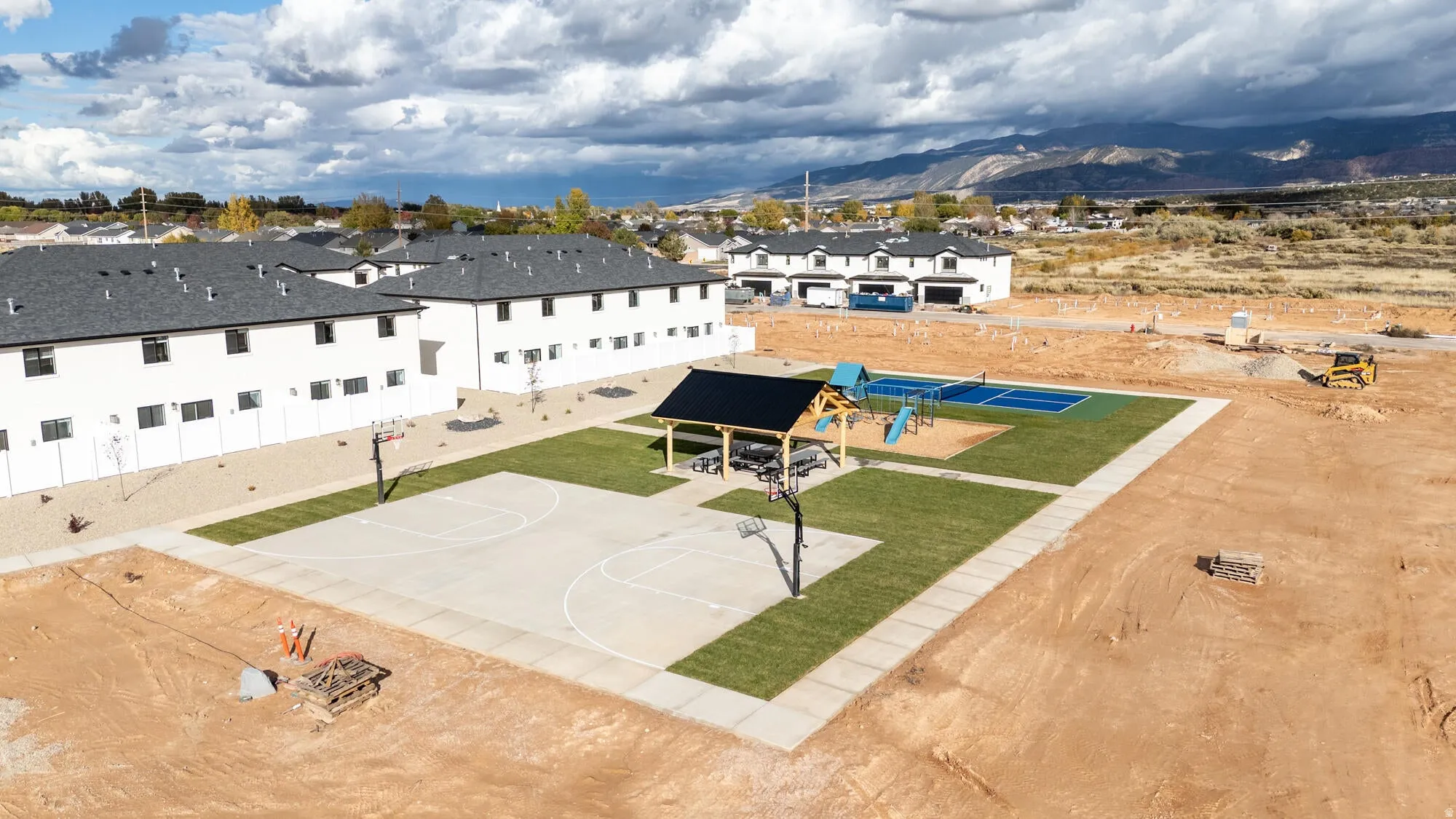 Recreational area featuring a basketball court, covered pavilion, and playground equipment, surrounded by newly sodded lawn areas