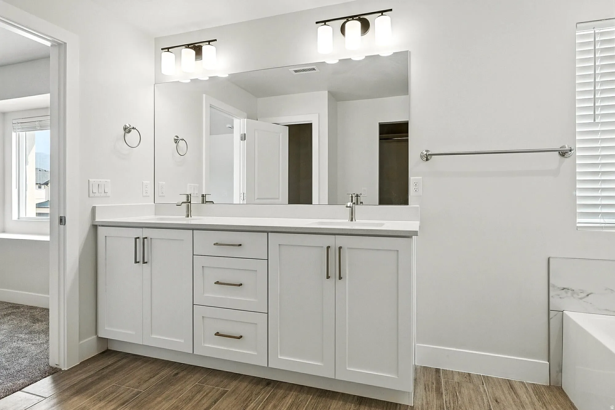 Dual sink vanity with white cabinetry, a light-toned countertop, and wood-finish flooring