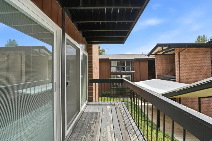 Private balcony featuring a wood-finish deck, black metal railing, and white-framed sliding glass doors