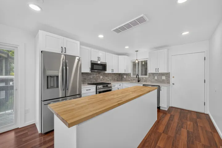 Kitchen featuring white shaker cabinetry, stainless steel appliances, a butcher block island, stone backsplash, and wood-finish flooring