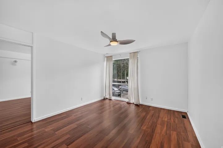 Spacious room featuring wood-finish flooring, white walls, and a contemporary ceiling fan with integrated lighting