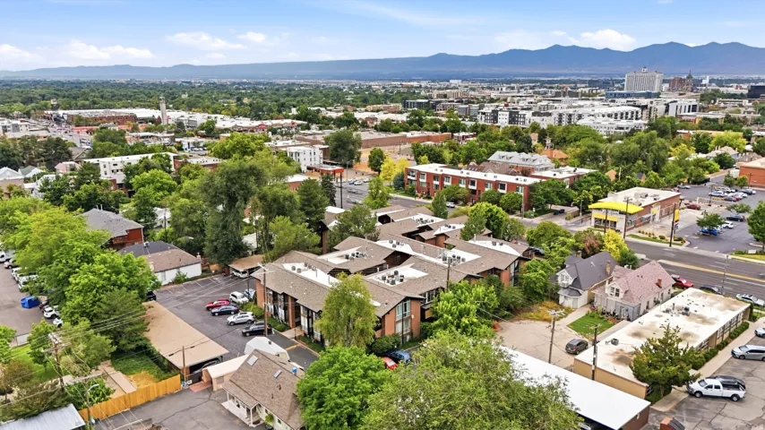 Aerial perspective of urban landscape featuring multiple structures with various rooflines, extensive tree canopy, and distant mountains
